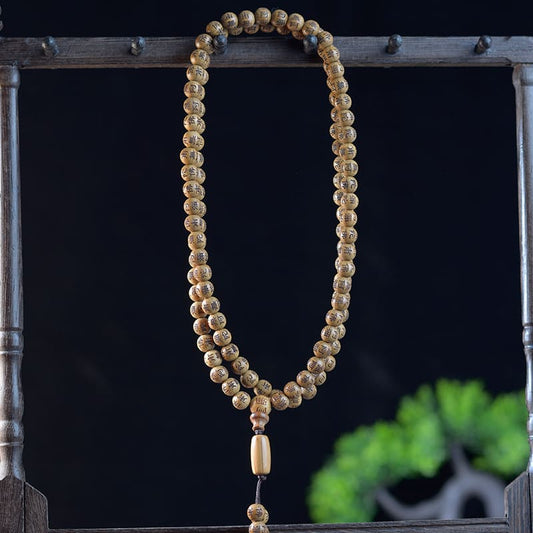 Close-up view of wooden prayer beads showing detailed mantra carvings and smooth finish