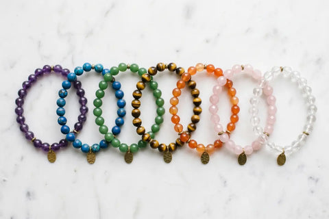 Seven natural gemstone chakra bracelet stones arranged in rainbow order on marble surface — complete guide by TrueZenBeads