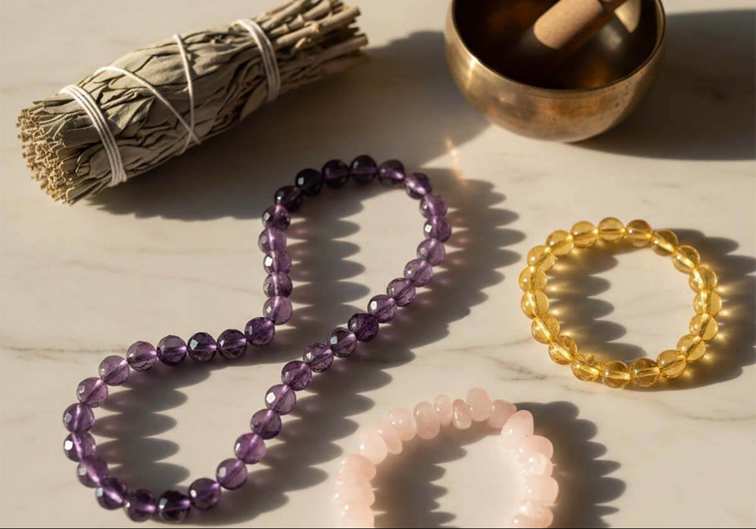 Natural crystal bracelets arranged with traditional cleansing tools like sage and singing bowl on marble surface