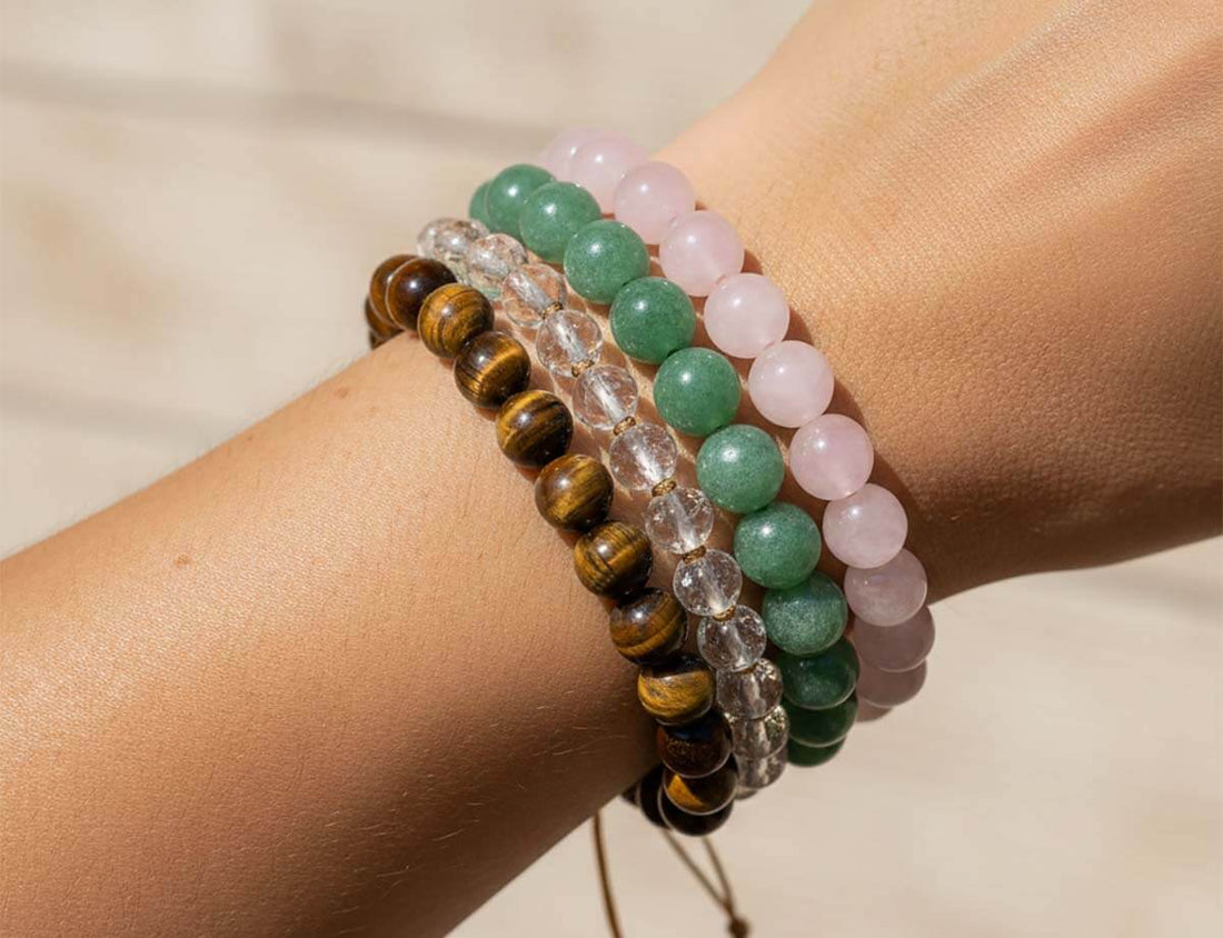 Person wearing natural stone bracelets showcasing variety of gemstones including tiger eye, rose quartz, and jade beads in natural light