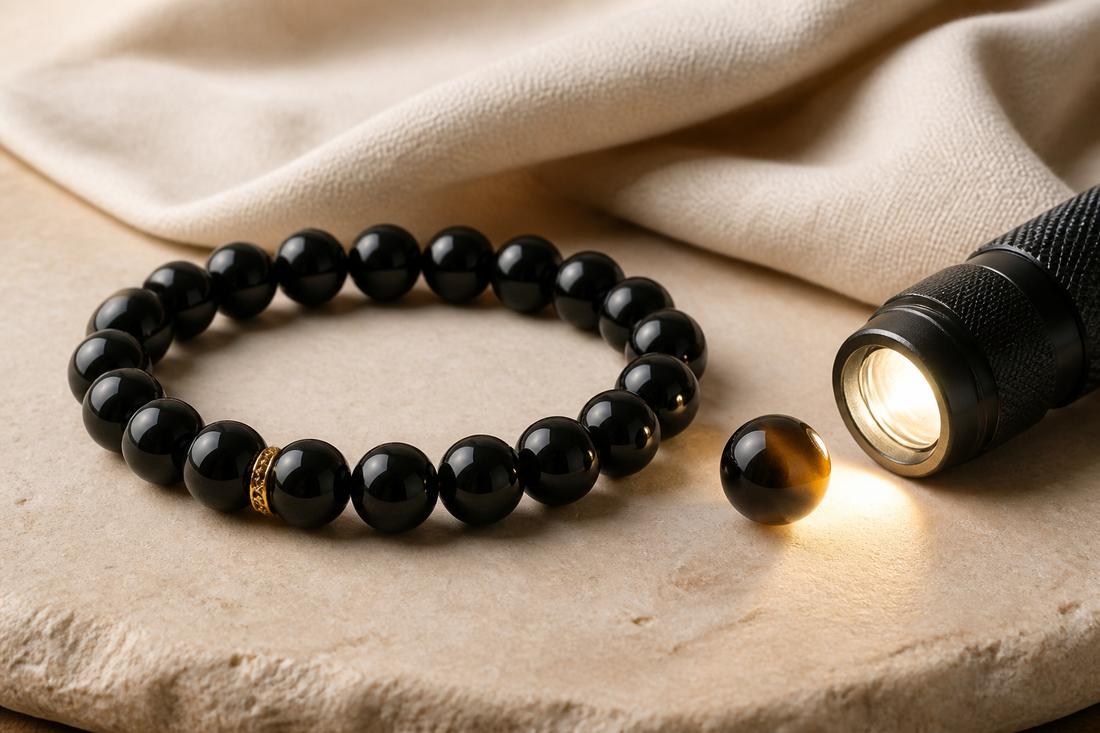 Black obsidian bracelet beside a flashlight showing faint smoky brown translucency at the edge of one bead