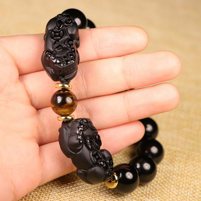 Close-up of double hand-carved Pixiu charms in black obsidian showing artisan detail and symmetrical design