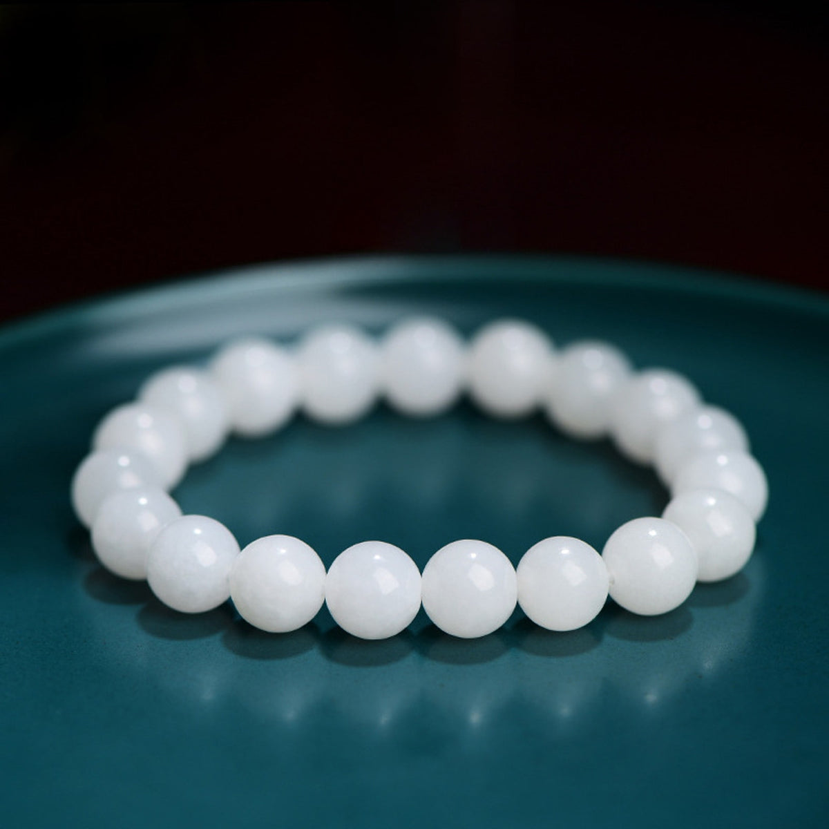 Hetian white jade bead bracelet on a teal display background