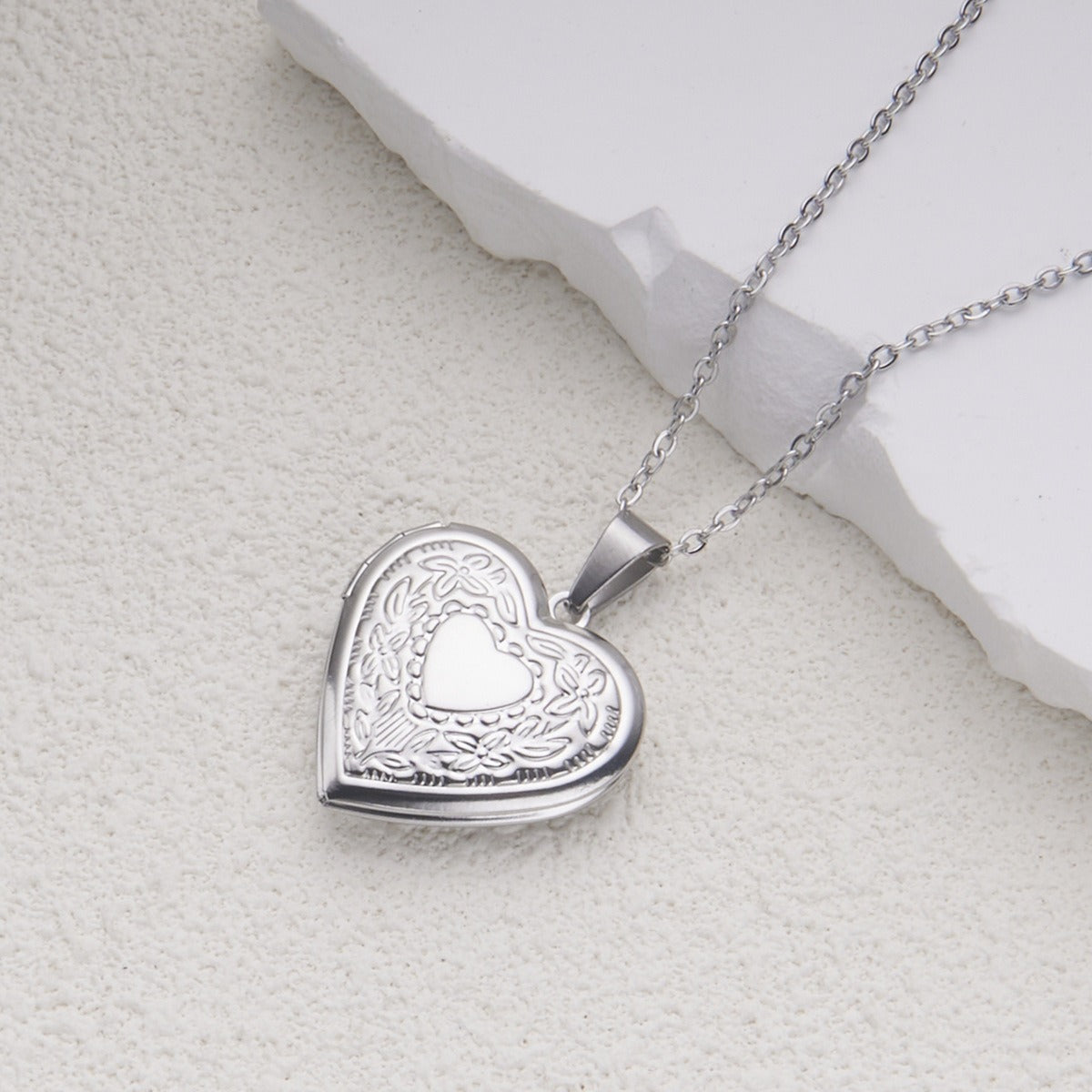 Silver heart locket necklace detail on a light stone background