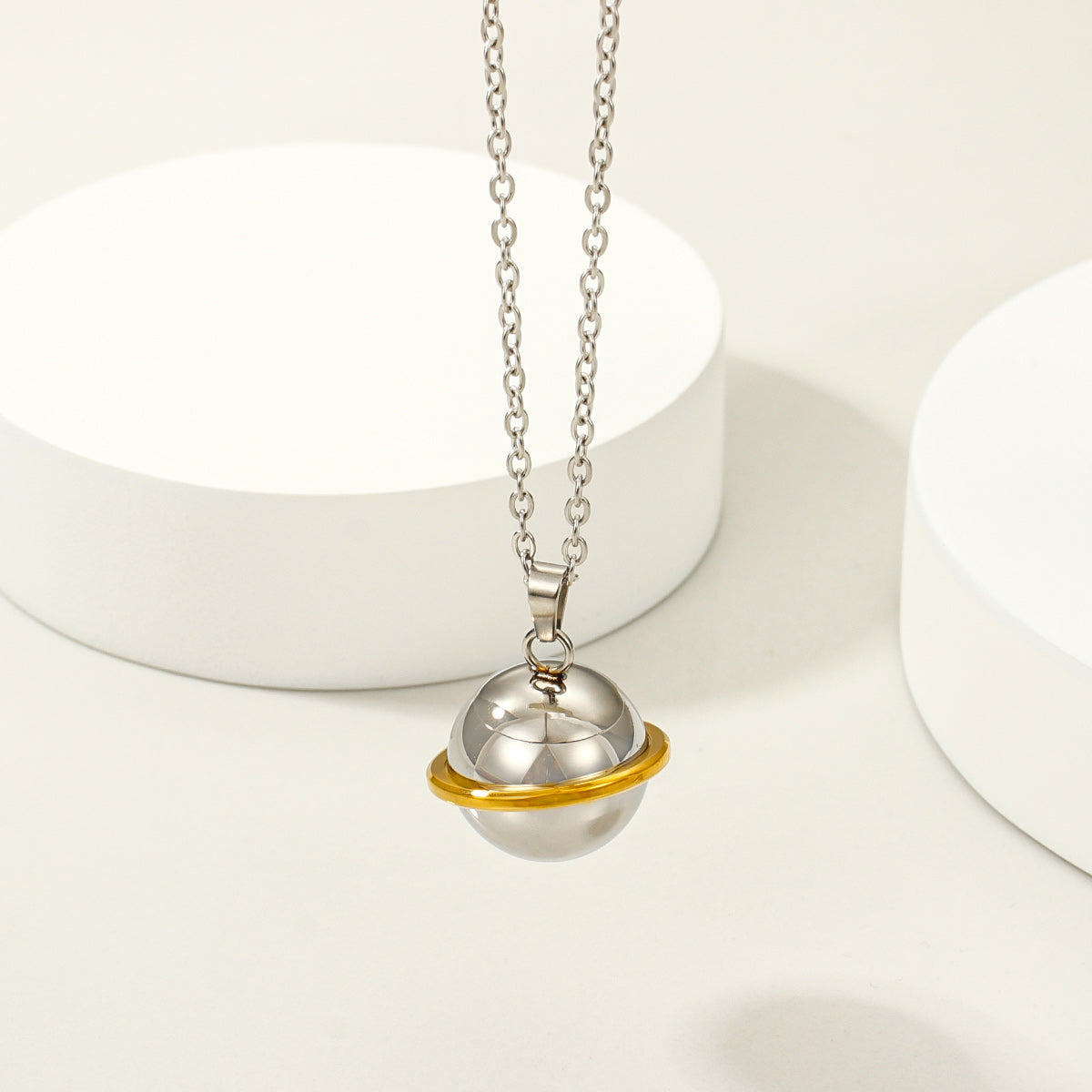 Stainless steel memorial orb necklace with gold-tone ring accent on a light display