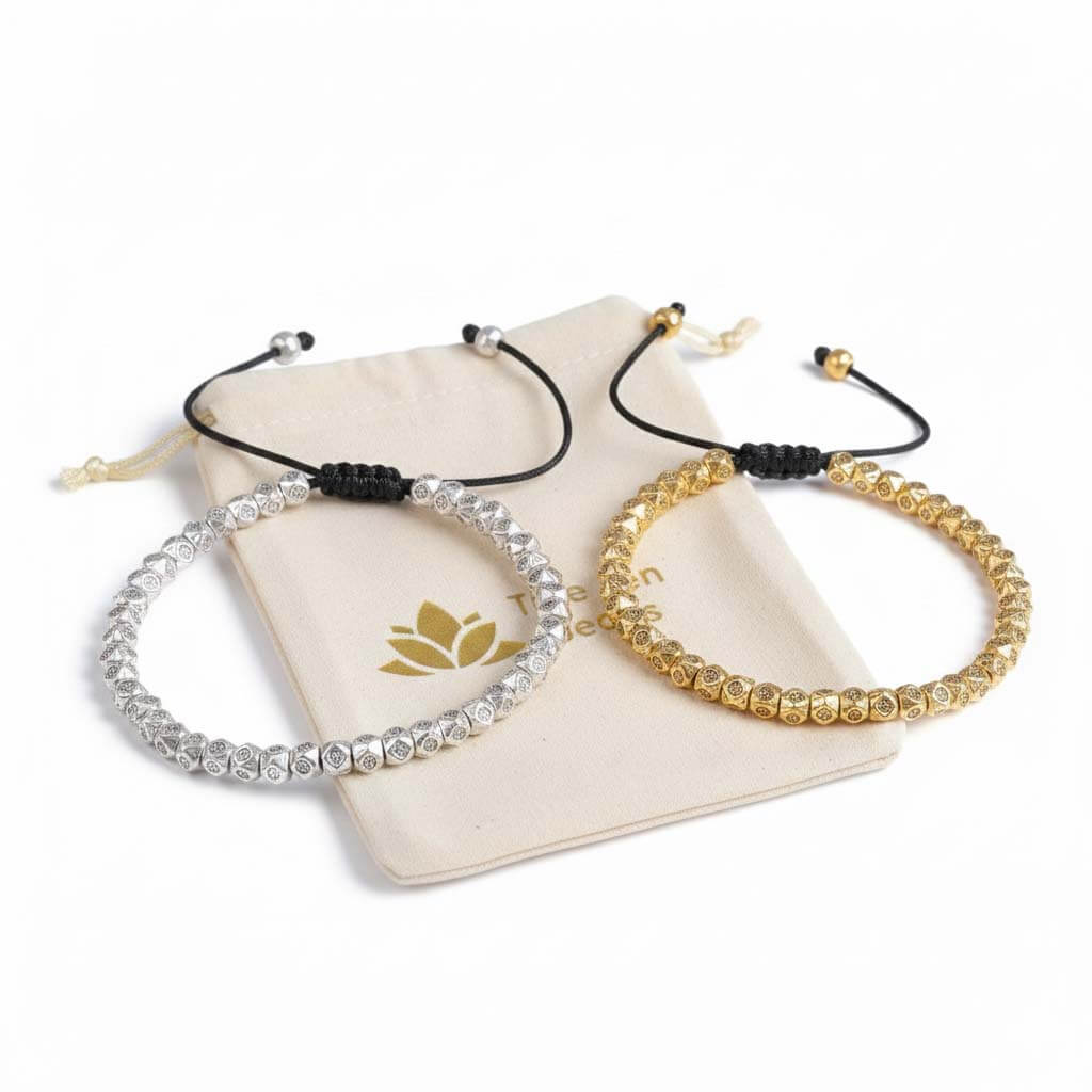 Two Tibetan mantra bracelets in gold and silver tones displayed on branded 
cream pouch with lotus flower logo ready for gift giving