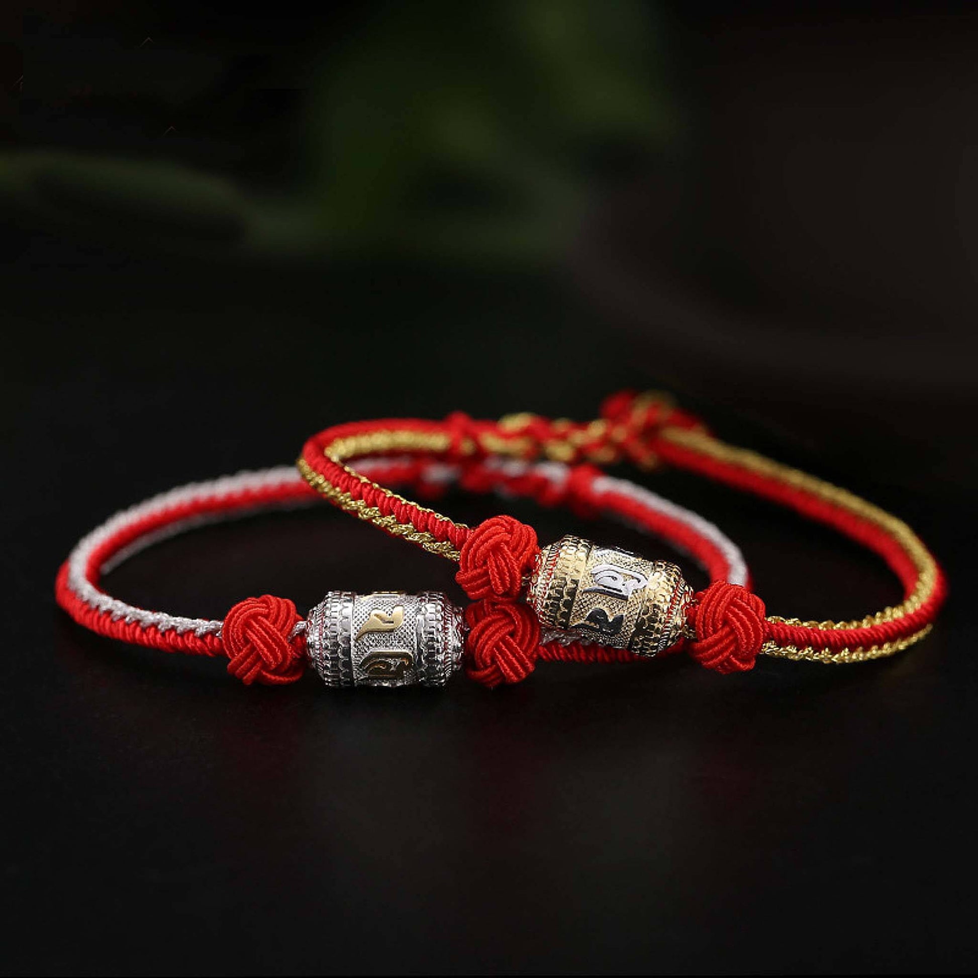 Tibetan red rope bracelets side by side showing gold-plated and silver-plated prayer wheel color comparison on black background