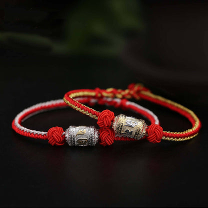Tibetan red rope bracelets side by side showing gold-plated and silver-plated prayer wheel color comparison on black background